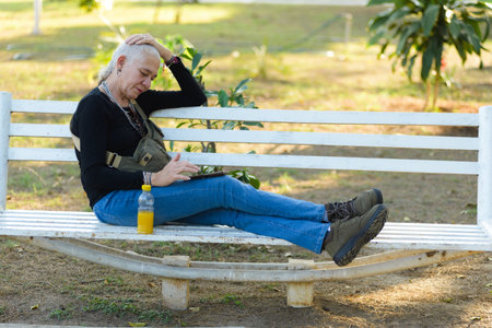 Middle-aged lesbian woman sitting on a park bench checks her cell phone.