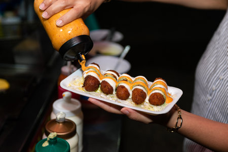 Close-up of a hand holding a styrofoam plate of fried croquettes.