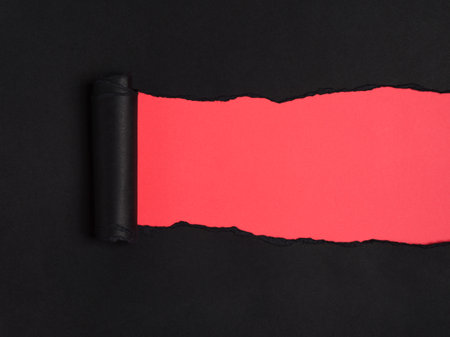 Ripped black rolled paper reveals a vibrant red underneath.の写真素材