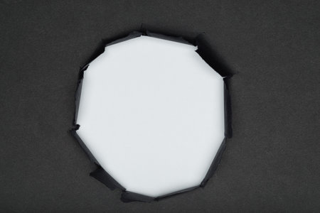 Center torn hole in black paper revealing white background, space for text.の写真素材