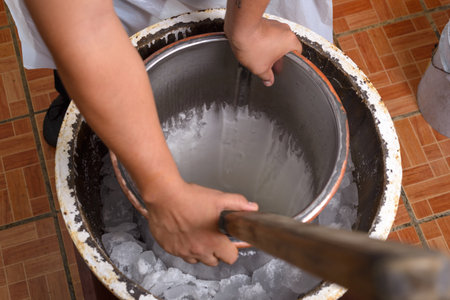 Male hands carefully churn a metal container of ice cream within a larger ice-filled vessel.