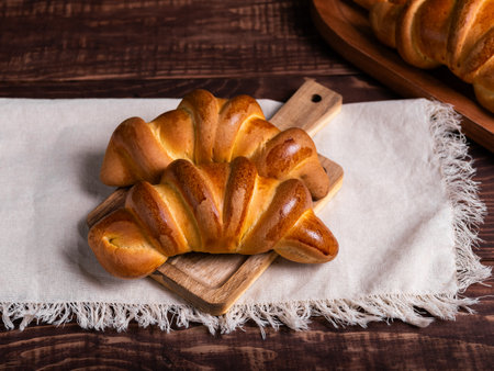 Two freshly baked croissants, golden brown and glistening, rest on a rustic wooden board atop a linen cloth.の写真素材