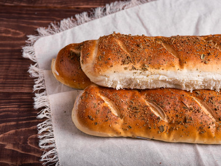 Three golden-brown herb-crusted loaves of bread rest on a linen cloth atop a dark wooden surface.