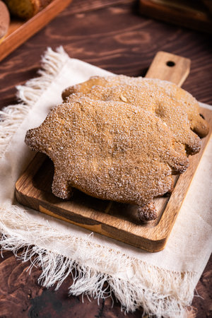 Two traditional pig-shaped bread, decorated with sugar crystals, rest on a rustic wooden board.