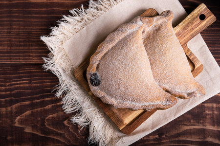 Close-up of two delicious empanadas dusted with sugar, resting on a rustic wooden board.