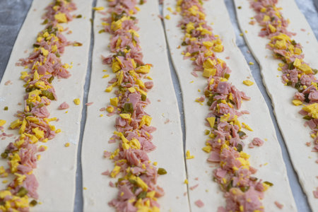 Close-up of raw puff pastry strips topped with diced ham, cheese, and jalapenos, ready for baking.の写真素材