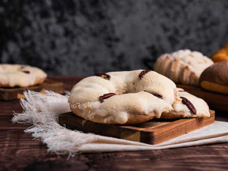Traditional Mexican sweet bread, garnished with pecans, rest on a rustic wooden board.