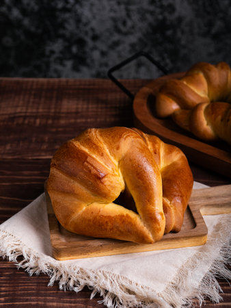 A freshly baked croissant rests on a rustic wooden board, placed on a linen cloth.の写真素材