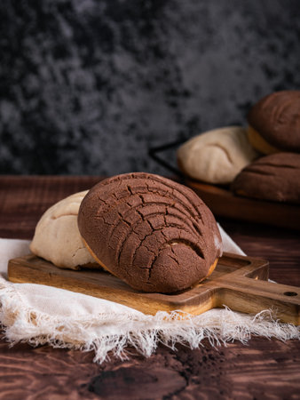 Close-up of two concha breads, one chocolate and one vanilla, resting on a wooden board.の写真素材