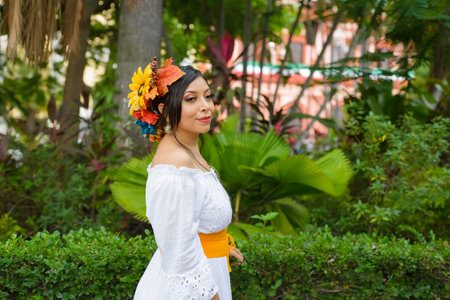 A woman in a white off-the-shoulder dress, adorned with a vibrant autumnal floral headpiece, stands gracefully amidst lush greenery.の写真素材