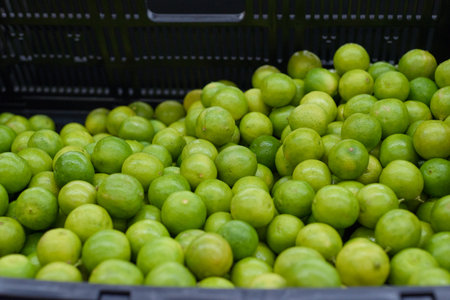 A close-up view of a brimming black plastic crate filled with numerous vibrant green limes.