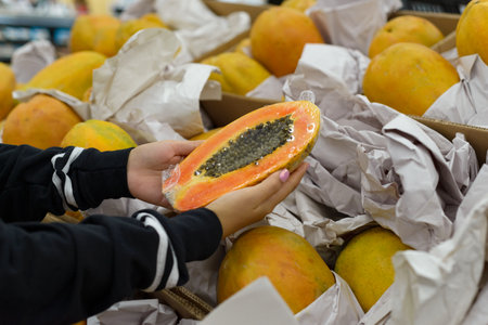 A person carefully chooses a ripe papaya from a display of fresh fruit at a grocery store.の写真素材