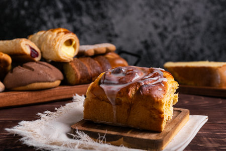 Sweet cinnamon roll on a wooden board on a rustic table, accompanied by an assortment of pastries.の写真素材