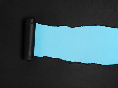 A piece of black paper is torn to reveal a strip of light blue underneath.の写真素材