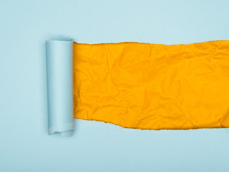 A vibrant image showscasing a torn piece of light blue paper revealing a layer of crumpled, bright yellow paper underneathの写真素材
