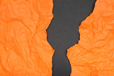 Crumpled orange tissue paper dramatically torn apart, revealing a dark gray background.の写真素材
