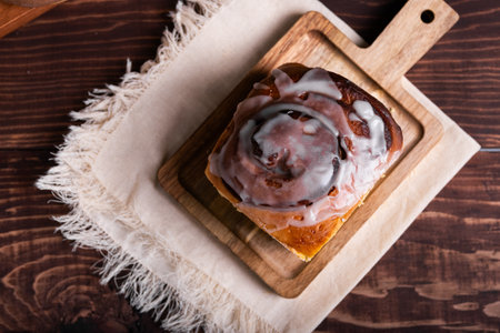 Sweet cinnamon roll on a wooden board on a rustic table, accompanied by an assortment of pastries.