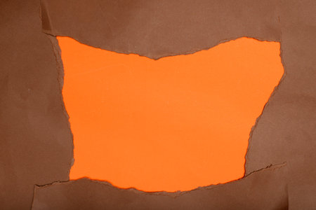 A bold orange backdrop framed by irregularly torn edges of deep brown paper.の写真素材