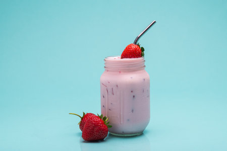 A mason jar brimming with a cool strawberry drink, garnished with fresh strawberries and a metal straw.の写真素材