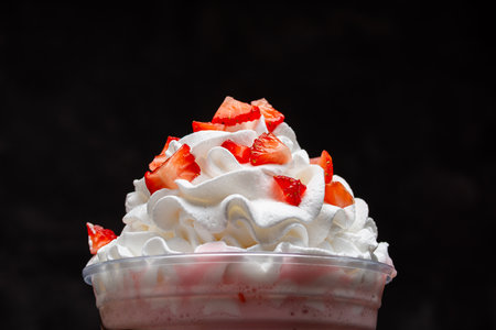 Strawberry milkshake in clear plastic cup on dark background.