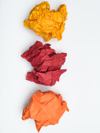 Three crumpled balls of paper, orange, red, and a lighter orange, are arranged vertically against a white background.の写真素材