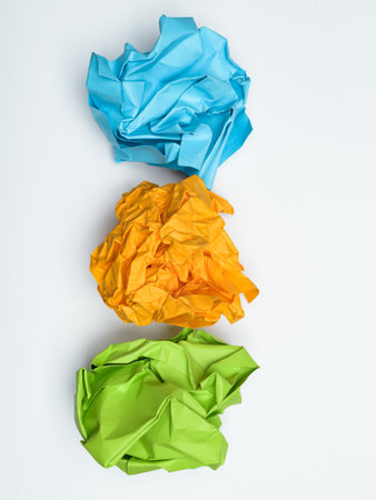 Three crumpled balls of brightly colored paper, blue, orange, and green, on white background.の写真素材