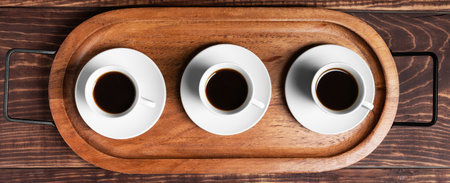 Three white espresso cups rest on matching saucers, arranged neatly on a rustic wooden serving tray