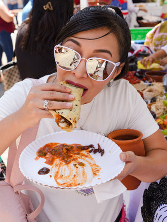A young woman enjoys a delicious taco at a vibrant Mexican street market.の写真素材