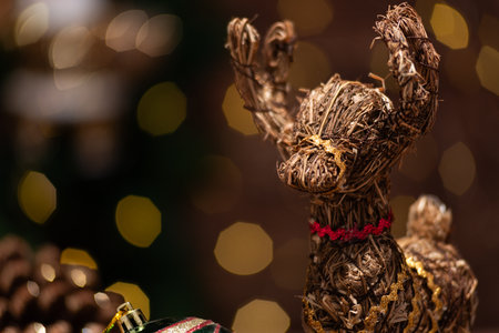 Close-up of a charming rustic reindeer ornament crafted from hay sits against a bokeh backdrop of warm Christmas lights.の写真素材