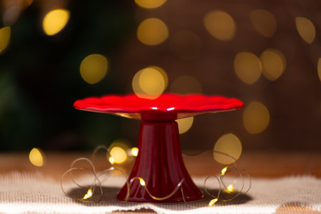 A red ceramic cake stand sits on burlap, encircled by warm fairy lights against a bokeh background.の写真素材