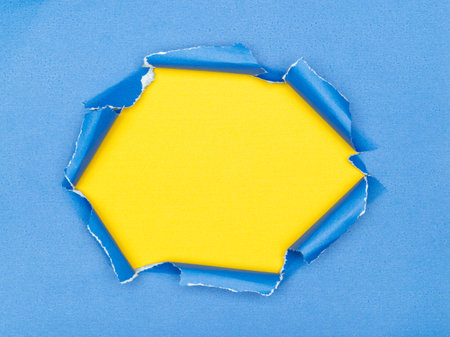 Torn blue paper with a bright yellow hexagon shaped hole in the middleの写真素材