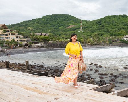 A woman stands on a wooden pier, looking out towards the ocean on a cloudy day.の写真素材