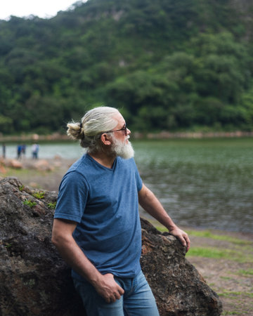 Contemplative Mature Man Leaning On Rock Overlooking Scenic Lake Landscapeの写真素材