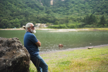 Contemplative Mature Man Leaning On Rock Overlooking Scenic Lake Landscapeの写真素材