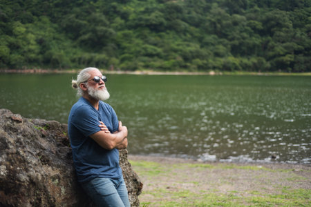 Contemplative Mature Man Leaning On Rock Overlooking Scenic Lake Landscapeの写真素材