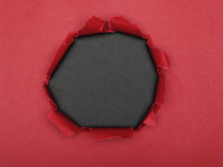 Torn hole in the center of a red paper on a black background.の写真素材