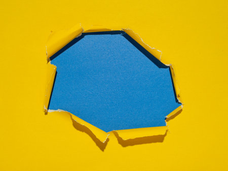 Torn hole in the center of a yellow paper on a blue background.の写真素材