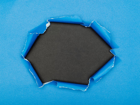 Torn hole in the center of a blue paper on a black background.の写真素材