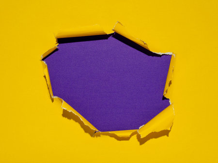 Torn hole in yellow paper with purple background underneath.の写真素材