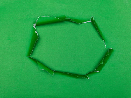 Torn hole in green paper with green background underneath.の写真素材