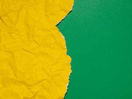 A bright yellow crumpled and torn paper against a solid green background.の写真素材