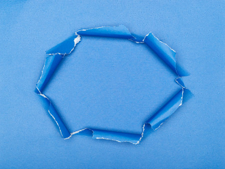 Torn hole in blue paper revealing a textured blue background.の写真素材