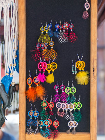 A collection of vibrant and unique handmade dreamcatcher earrings featuring colorful feathers, displayed on a wooden stand.の写真素材