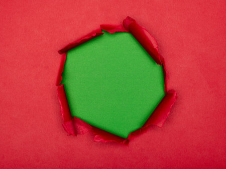 Torn hole in red paper revealing a textured green background.の写真素材