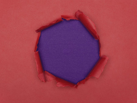 Torn hole in red paper revealing a textured purple background.の写真素材