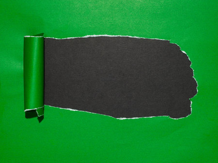 Torn green paper revealing a dark surface underneath.の写真素材