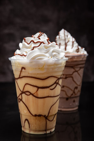 Vanilla milkshake with chocolate syrup in clear plastic cup on dark background.の写真素材