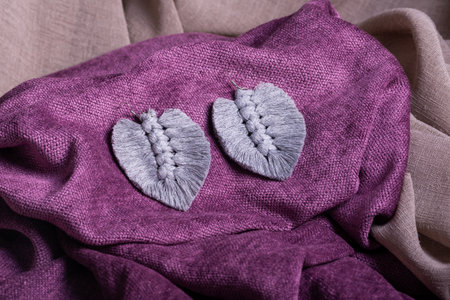 A close up of two handmade macrame earrings in the shape of leaves, resting on a vibrant purple textured fabric.の写真素材