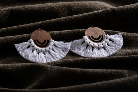 A close-up of handmade macrame tassel earrings with wooden circle detail, displayed on a textured fabric surface.の写真素材