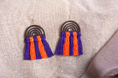 A pair of handmade earrings featuring a wooden rainbow shaped top with purple and orange macrame tassel fringe.の写真素材